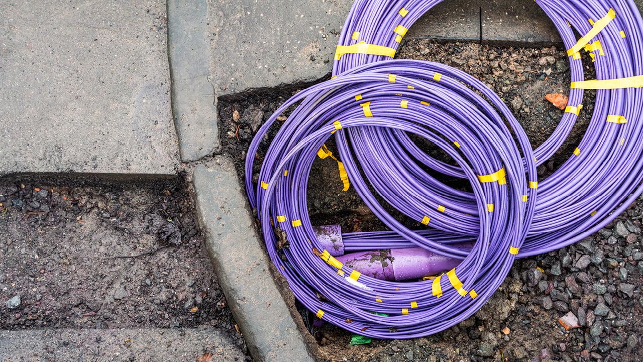 Coils of purple fibre-optic cable positioned beside a roadside excavation during broadband network installation.